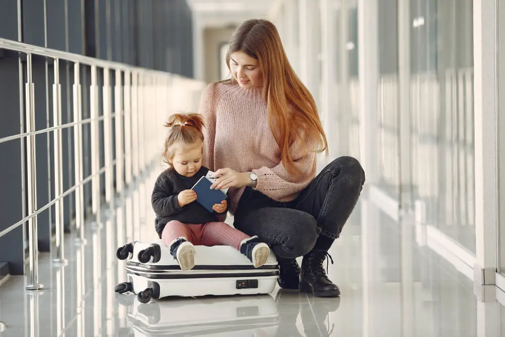 Viajando tranquilo com seu bebê: Mulher com filha em cima da mala esperando o avião no aeroporto.